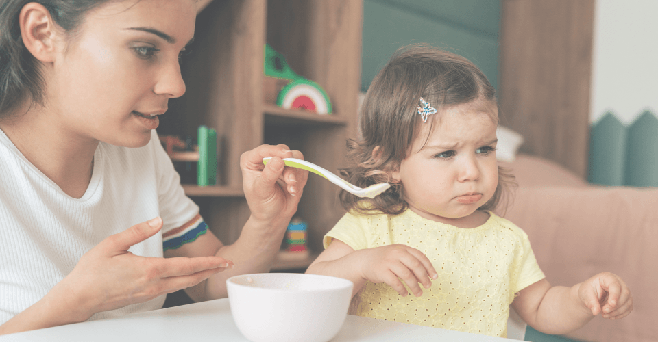 une employée de crèche qui nourrit un bébé fille à la cuillère qui est degoutée